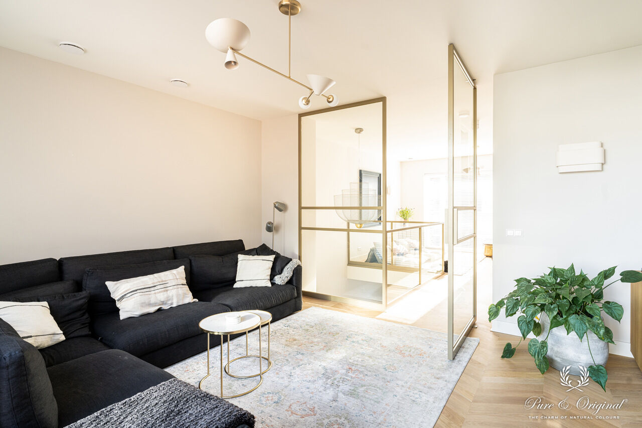 Interieur met een blauwe zetel in een wit interieur, gecombineerd met gouden accenten zoals deurframes en salontafel. Houten materialen zorgen voor warmte en balans in een elegante, lichte ruimte.