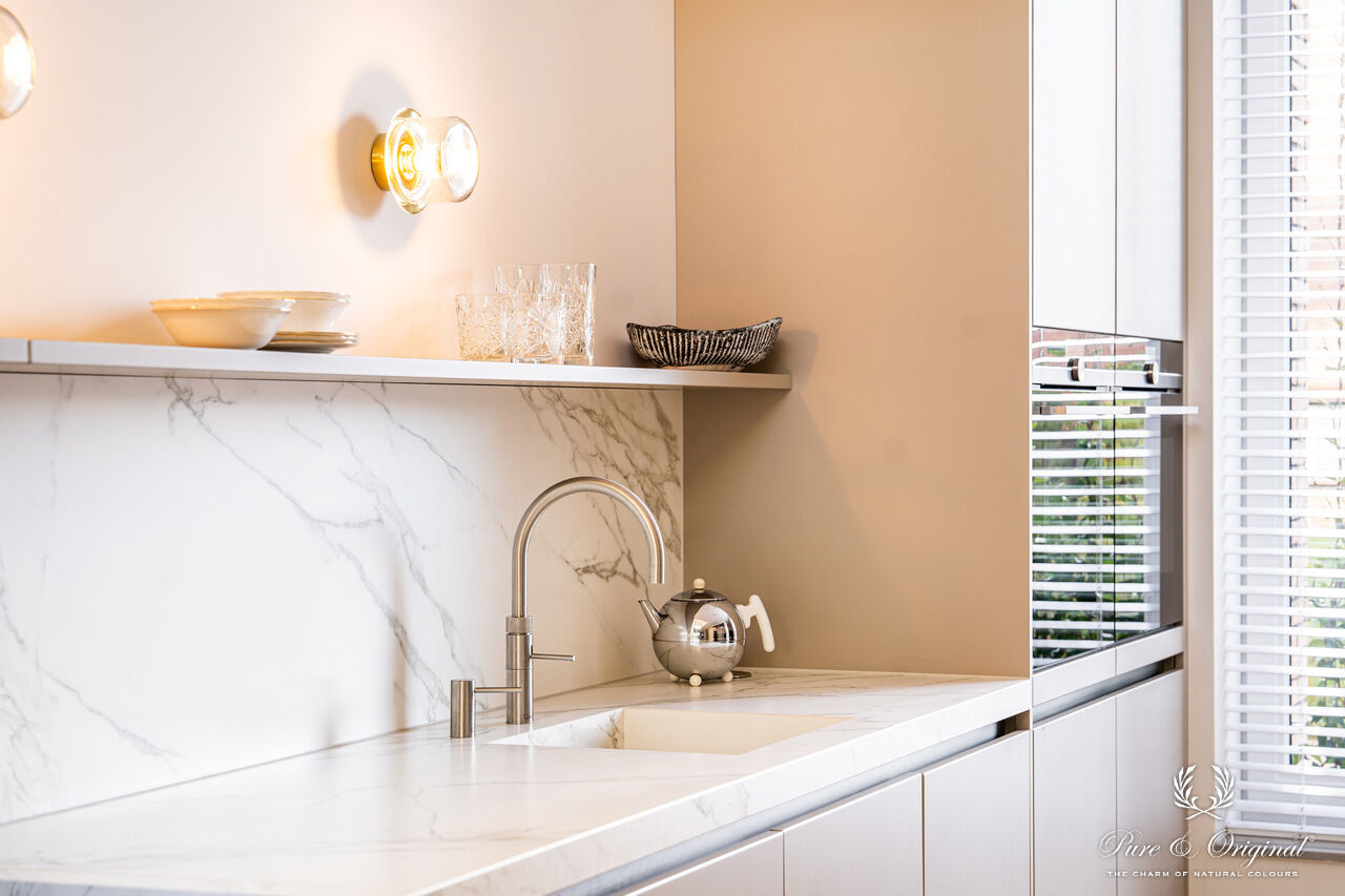 Interieur met een blauwe zetel in een wit interieur, gecombineerd met gouden accenten zoals deurframes en salontafel. Houten materialen zorgen voor warmte en balans in een elegante, lichte ruimte.