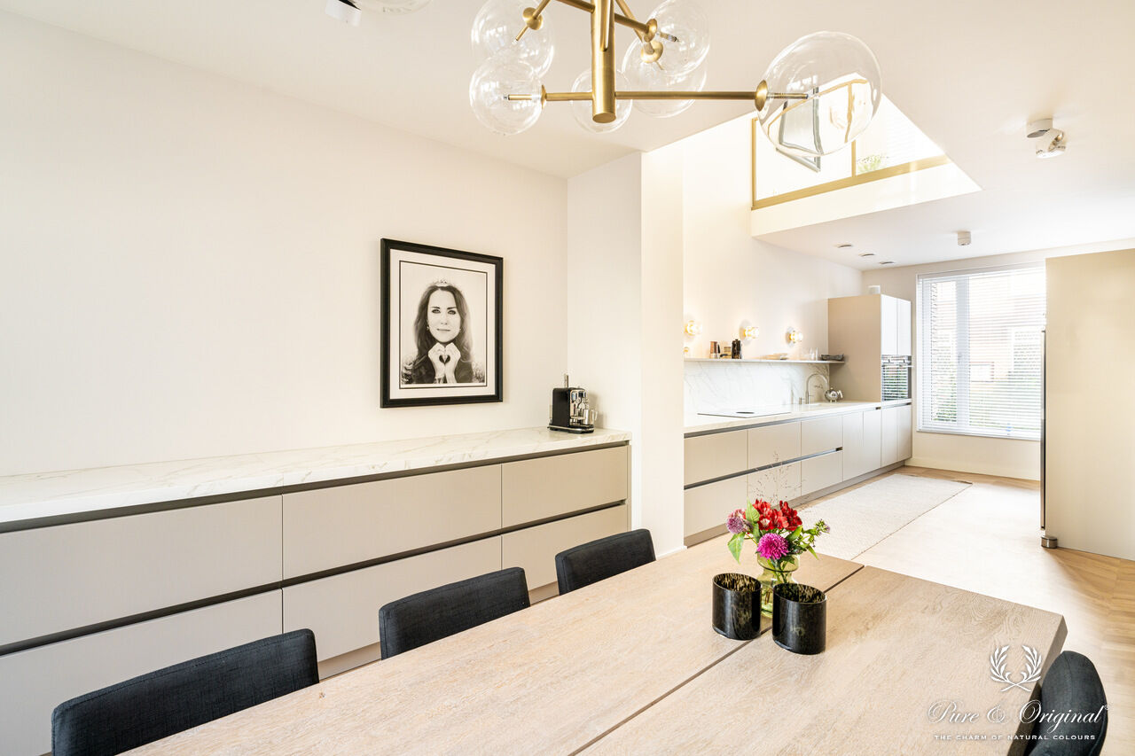 Interieur met een blauwe zetel in een wit interieur, gecombineerd met gouden accenten zoals deurframes en salontafel. Houten materialen zorgen voor warmte en balans in een elegante, lichte ruimte.
