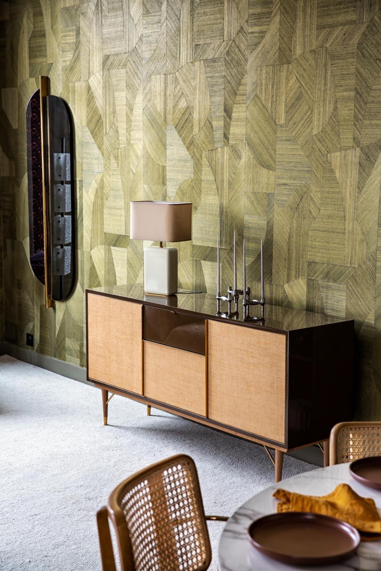 Showroom appartement RED met geometrisch groen geweven Arte Walls behang, blauwe zetel, donker roodbruin houten salontafel en planten. Modern interieur met warme materialen en natuurlijke accenten.