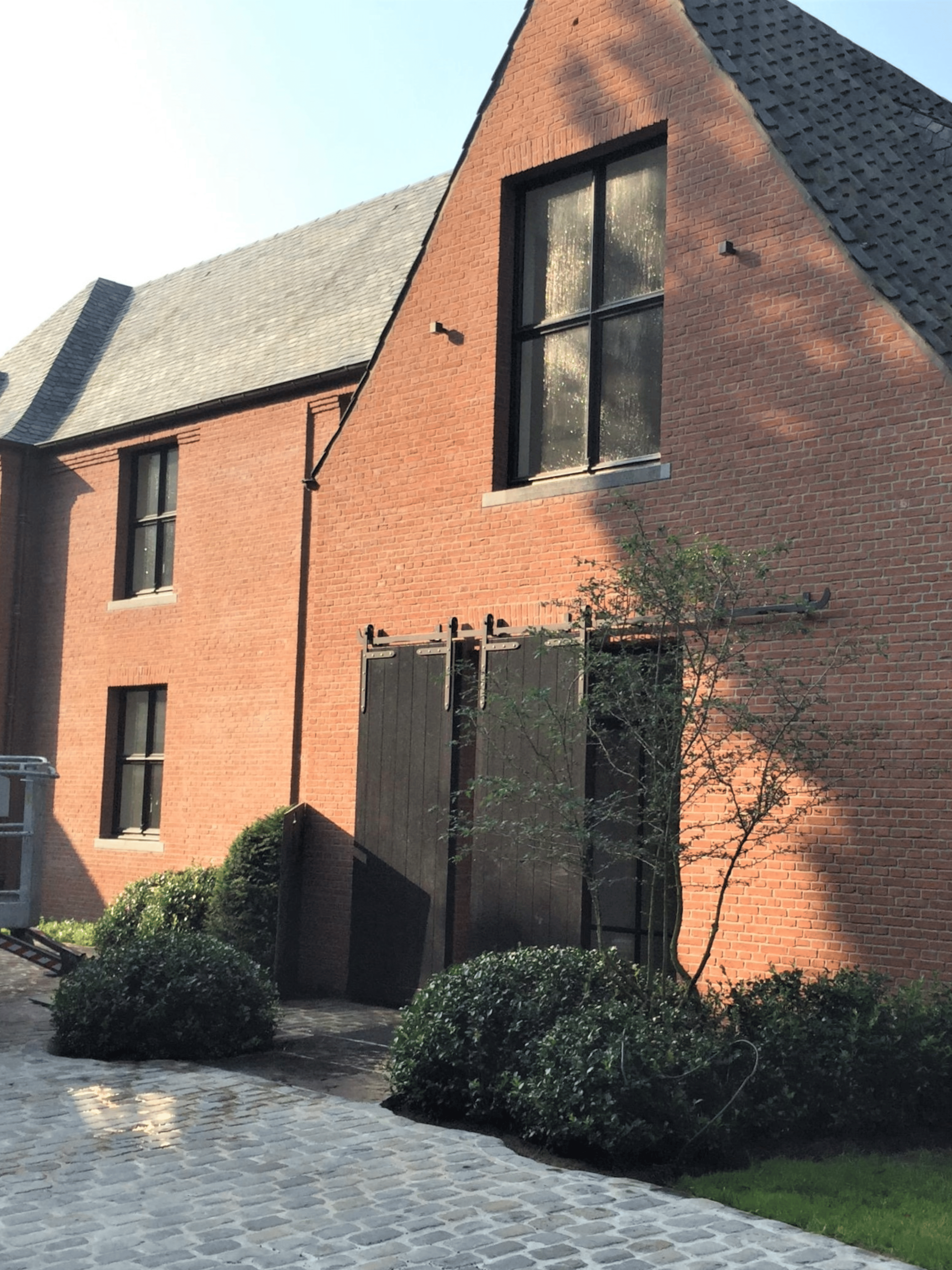 Moderne hoeve met een witte gekaleide gevel, grote zwarte aluminium raampartijen, een zwart dak en een groene tuin met weelderige beplanting. Duurzame kalei zorgt voor een strakke en tijdloze gevelafwerking.