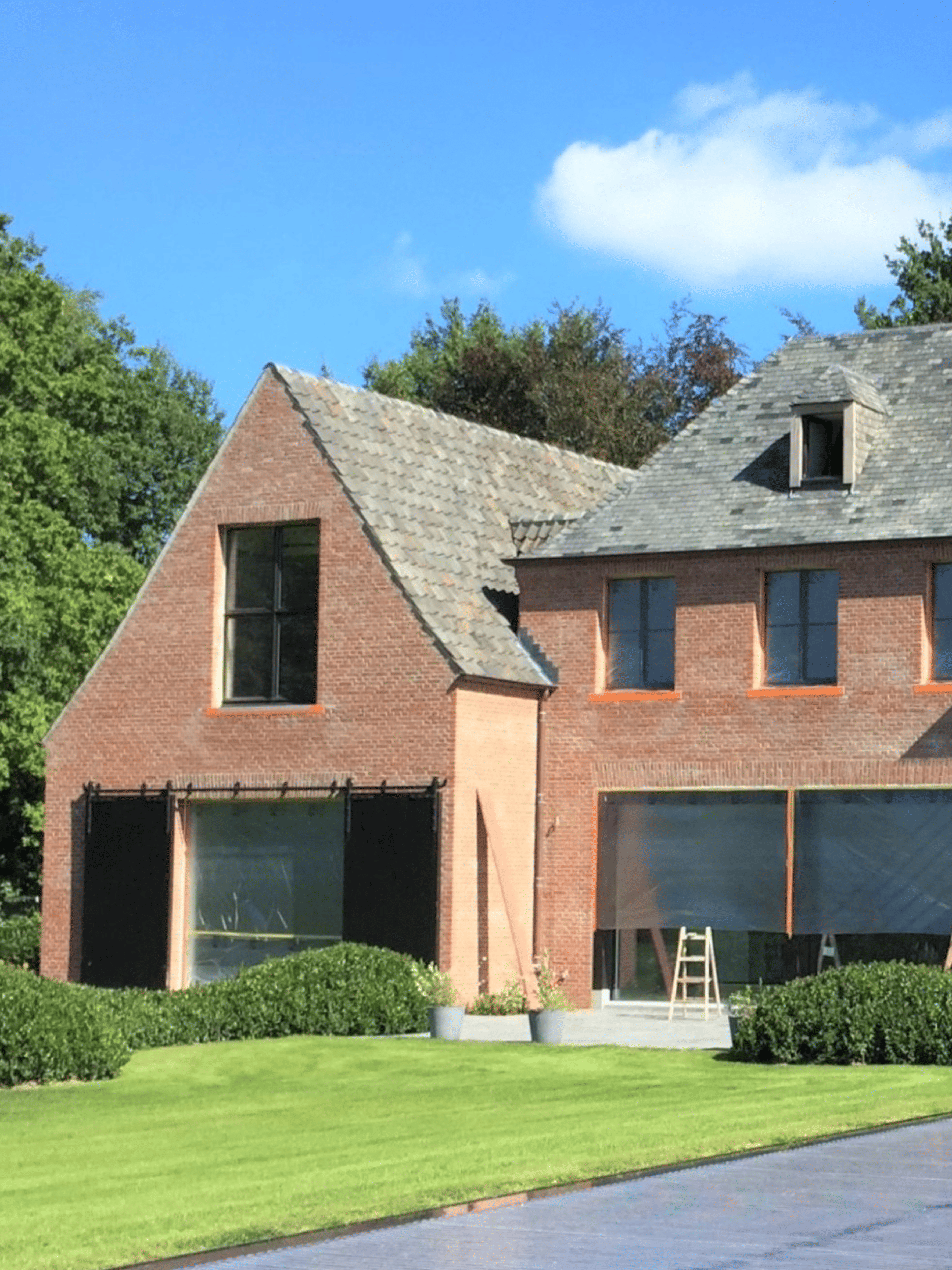 Moderne hoeve met een witte gekaleide gevel, grote zwarte aluminium raampartijen, een zwart dak en een groene tuin met weelderige beplanting. Duurzame kalei zorgt voor een strakke en tijdloze gevelafwerking.