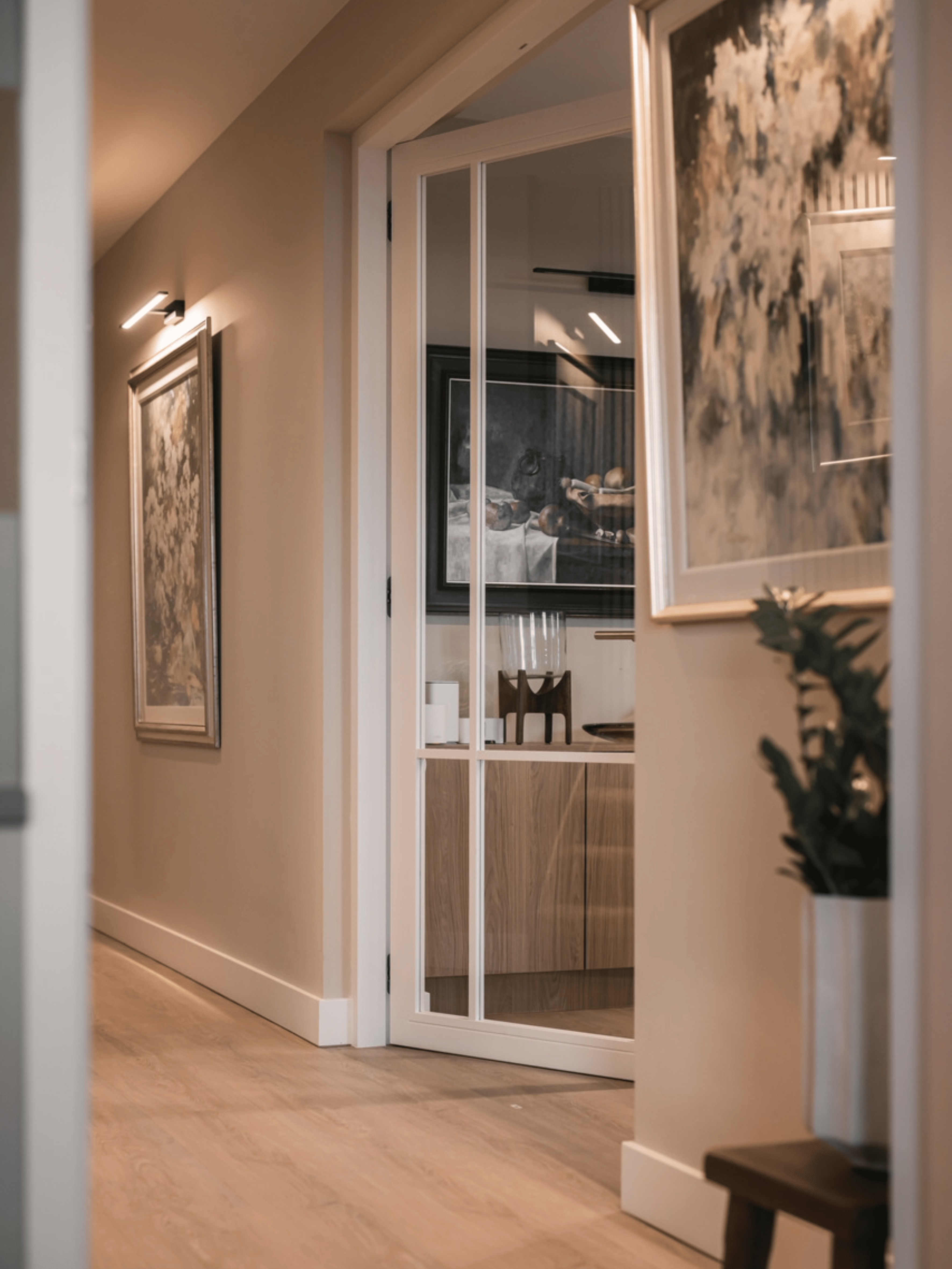 Strak landelijk interieur afgewerkt met verf van Pure & Original in zachte natuurtinten. Houten vloer zorgt voor warmte, gecombineerd met witte sierprofielen, grote schilderijen als eyecatcher en groene planten voor een natuurlijke uitstraling.
