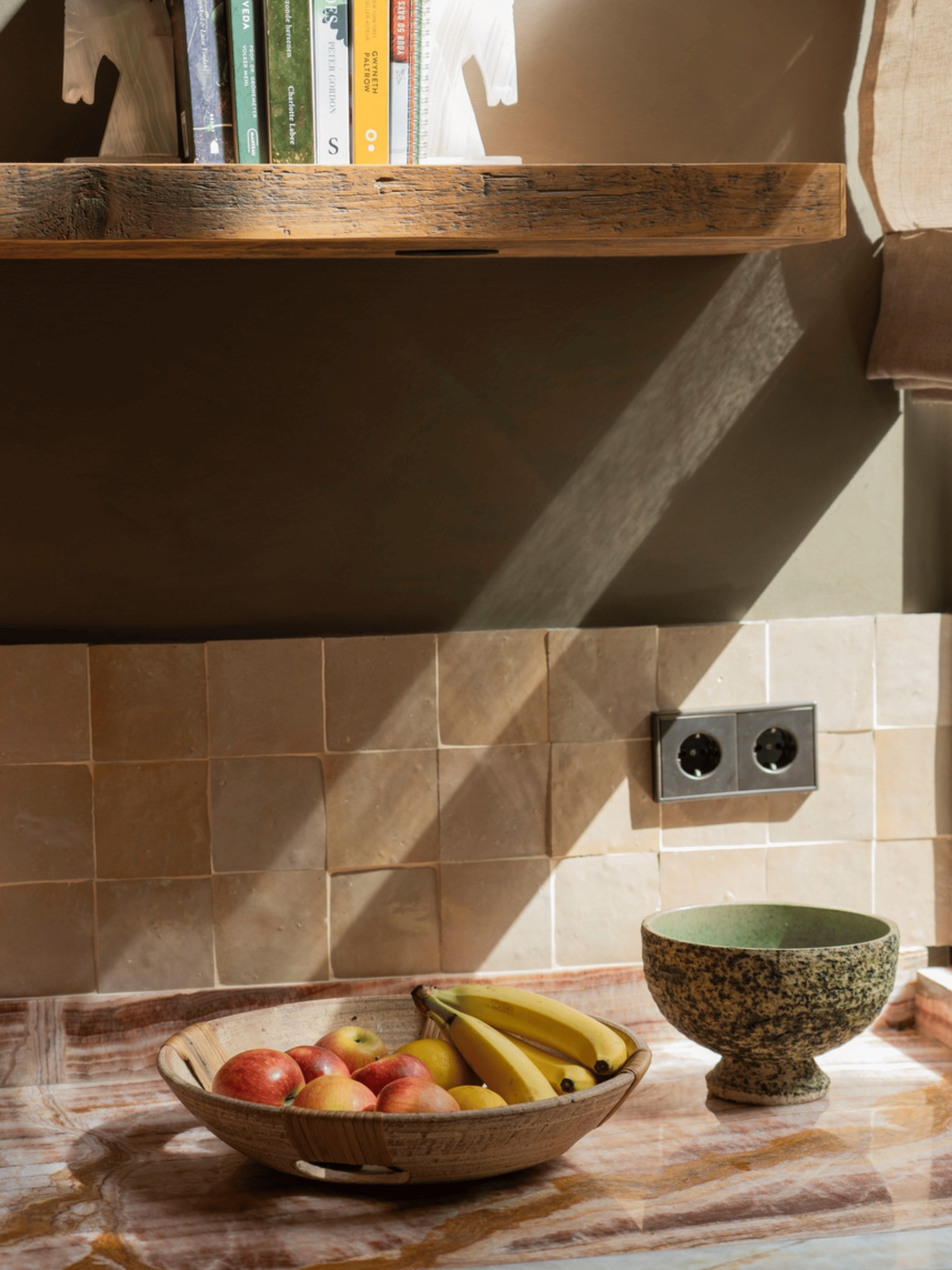 Landelijke eetkamer met bordeauxkleurige keukenkasten, zacht beige-groene wandafwerking en een houten eettafel. Witte rozen als decoratie zorgen voor een frisse en elegante, warme sfeer in het interieur.