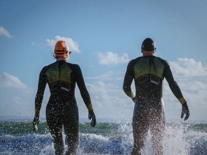 Triathlètes en combinaison néoprène Zone3 entrant dans l’eau, location de wetsuits
